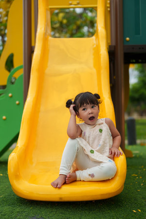 happy toddler baby girl sliding and playing at outdoor playground