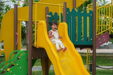 happy toddler baby girl sliding and playing at outdoor playgroundの写真素材