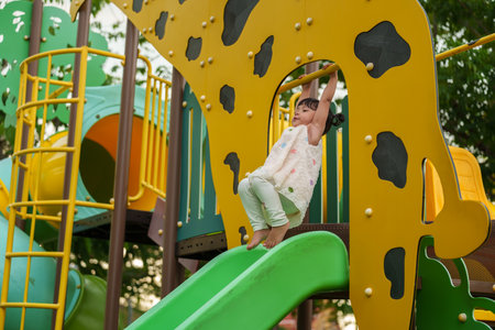 happy toddler girl hanging the yellow bar by her hand at outdoor playground in the parkの写真素材