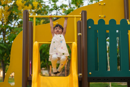 happy toddler girl hanging the yellow bar by her hand at outdoor playground in the parkの写真素材