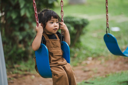cheerful toddler girl playing on a swingの写真素材