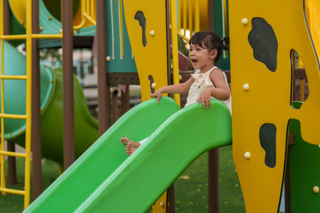 happy toddler baby girl sliding and playing at outdoor playgroundの写真素材