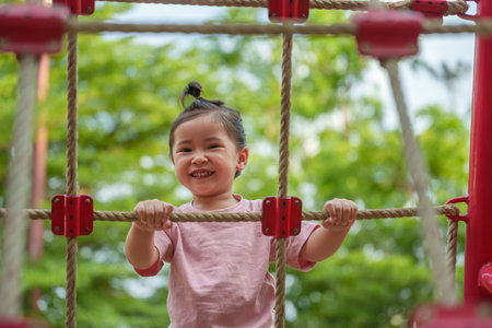 happy toddler girl playing with climbing ropes net at a outdoor playground in the parkの写真素材