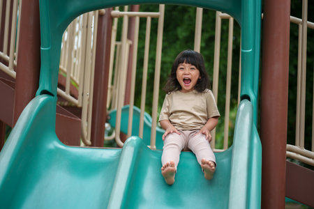 happy toddler baby girl sliding and playing at outdoor playgroundの写真素材