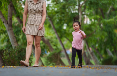 toddler girl walking with her mother on sidewalk at parkの写真素材