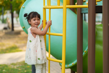happy toddler girl playing and climbing on outdoor playground at the parkの写真素材