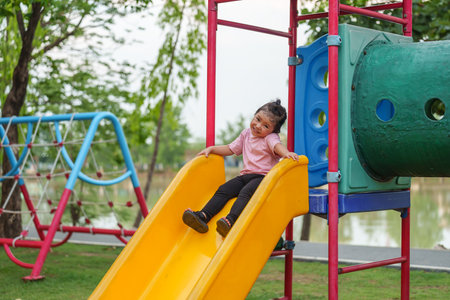 happy toddler baby girl sliding and playing at outdoor playgroundの写真素材
