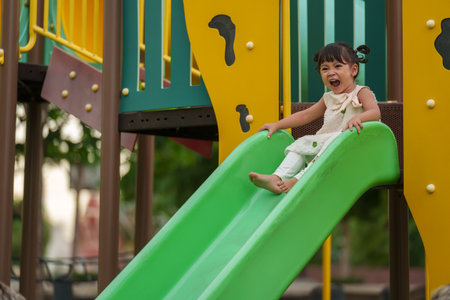 happy toddler baby girl sliding and playing at outdoor playgroundの写真素材
