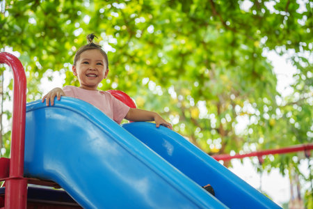 happy toddler baby girl sliding and playing at outdoor playgroundの写真素材