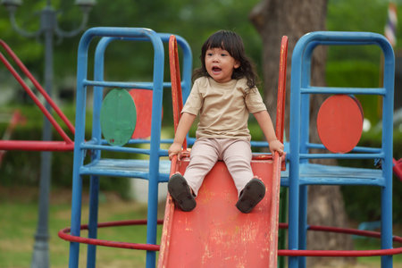 happy toddler baby girl sliding and playing at outdoor playgroundの写真素材