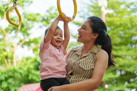 mother holding her daughter to hanging on playground rings in the parkの写真素材