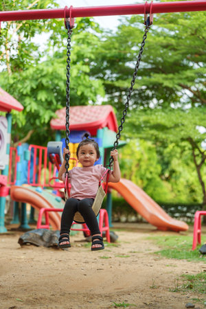 cheerful toddler girl playing on a swing at outdoor playgroundの写真素材