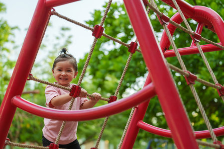 happy toddler girl playing with climbing ropes net at a outdoor playground in the parkの写真素材