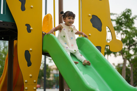 happy toddler baby girl sliding and playing at outdoor playgroundの写真素材