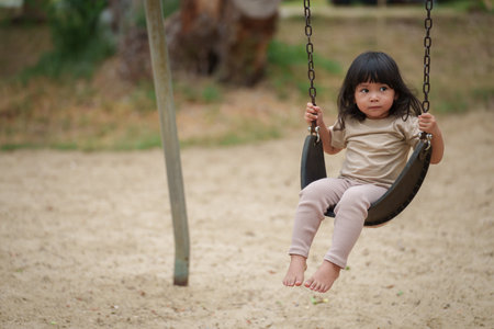 cheerful toddler girl playing on a swing at outdoor playground
