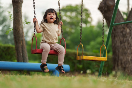 cheerful toddler girl playing on a swing at outdoor playgroundの写真素材