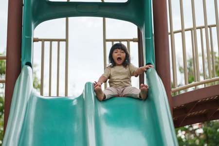 happy toddler baby girl sliding and playing at outdoor playgroundの写真素材