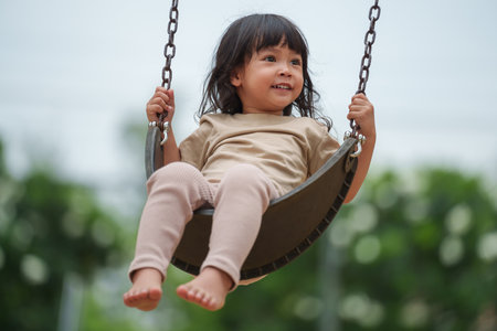 cheerful toddler girl playing on a swing at outdoor playgroundの写真素材