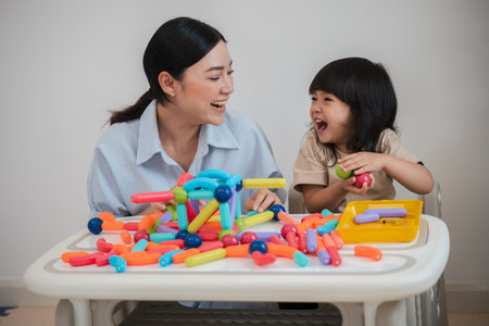 toddler girl and her mother playing colorful magnetic construction toy at homeの写真素材