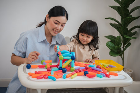 toddler girl and her mother playing colorful magnetic construction toy at home