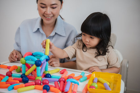 toddler girl and her mother playing colorful magnetic construction toy at home