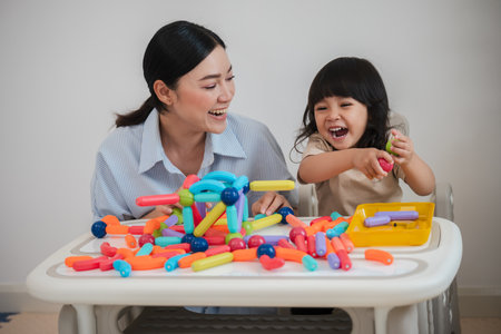 toddler girl and her mother playing colorful magnetic construction toy at homeの写真素材