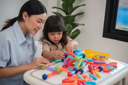 toddler girl and her mother playing colorful magnetic construction toy at homeの写真素材