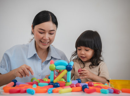 toddler girl and her mother playing colorful magnetic construction toy at homeの写真素材