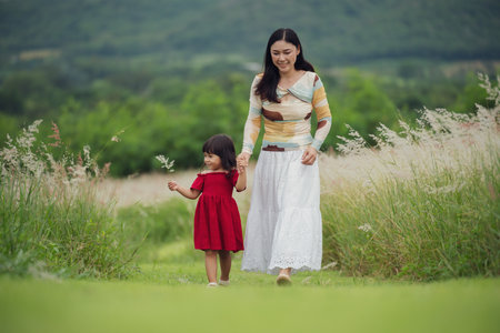 happy mother walking with her toddler girl on a grass fieldの写真素材