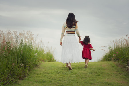 mother walking with her toddler girl on a grass fieldの写真素材