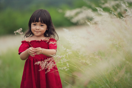 cheerful toddler girl in red dress playing grass flower in fieldの写真素材