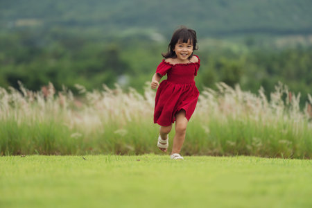 happy toddle girl in red dress running on a grass fieldの写真素材