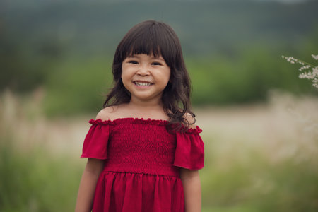 cheerful toddler girl in red dress playing in a grass fieldの写真素材