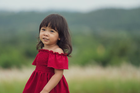 cheerful toddler girl in red dress playing in a grass fieldの写真素材