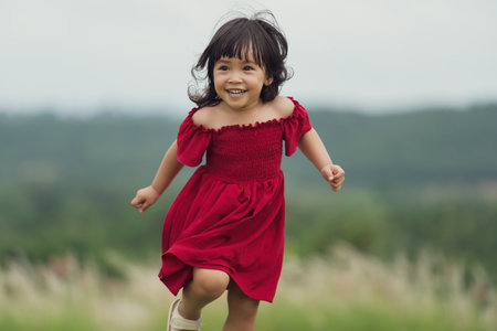happy toddle girl in red dress running on a grass fieldの写真素材