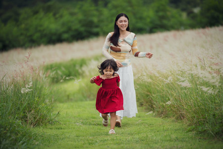 toddler girl running with her mother on a grass fieldの写真素材