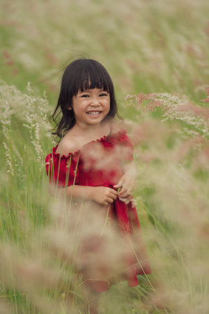 cheerful toddler girl in red dress playing grass flower in fieldの写真素材