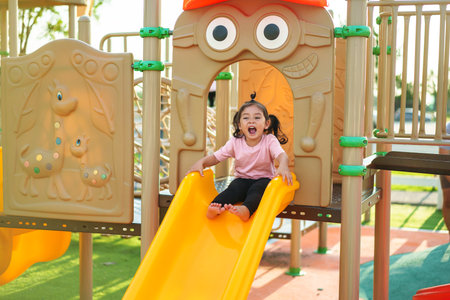 happy toddler baby girl sliding and playing at outdoor playgroundの写真素材