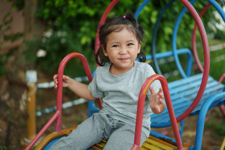 happy toddler baby girl sliding and playing at outdoor playgroundの写真素材