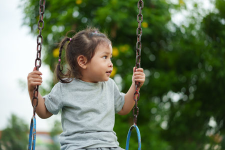 cheerful toddler girl playing on a swing at outdoor playgroundの写真素材