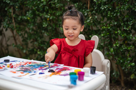 happy toddler girl painting watercolor in a paper at backyard.の写真素材