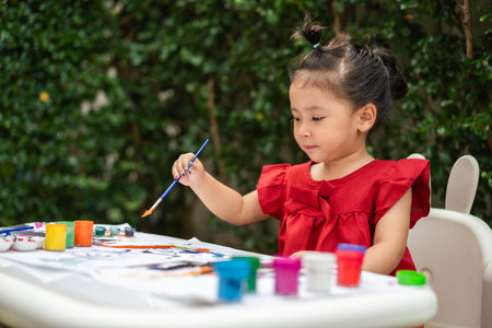 happy toddler girl painting watercolor in a paper at backyard.の写真素材