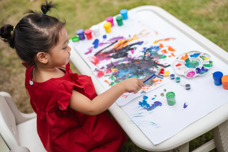 happy toddler girl painting watercolor in a paper at backyard.の写真素材