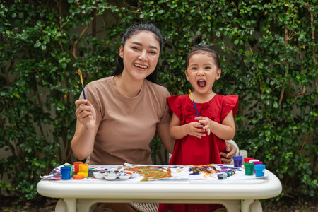 happy mother and toddler girl painting watercolor in a paper at backyard.の写真素材
