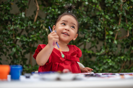 happy toddler girl painting watercolor in a paper at backyard.の写真素材