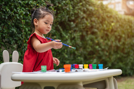 happy toddler girl painting watercolor in a paper at backyard.の写真素材
