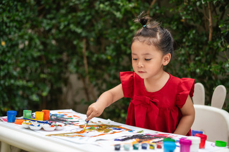happy toddler girl painting watercolor in a paper at backyard.の写真素材