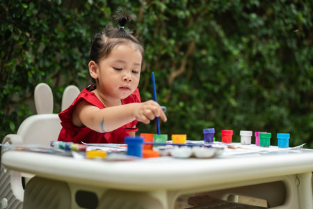 happy toddler girl painting watercolor in a paper at backyard.の写真素材