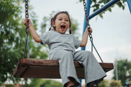 cheerful toddler girl playing on a wooden swing at playgroundの写真素材
