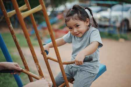 cheerful toddler girl playing on a double swing with friend at outdoor playgroundの写真素材